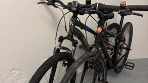 Dos bicicletas estacionadas junto a una pared en una habitación con piso gris y paredes blancas.