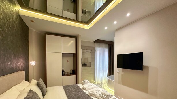 A modern hotel room with a large bed, a TV mounted on the wall, and a bathroom visible through a glass door. - Suite with jacuzzi near Vatican (Room 1) (Roma)