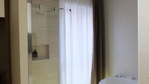 A modern bathroom with a glass-enclosed shower, a large bathtub, and neatly folded towels on a wooden floor. - Suite with jacuzzi near Vatican (Room 1) (Roma)