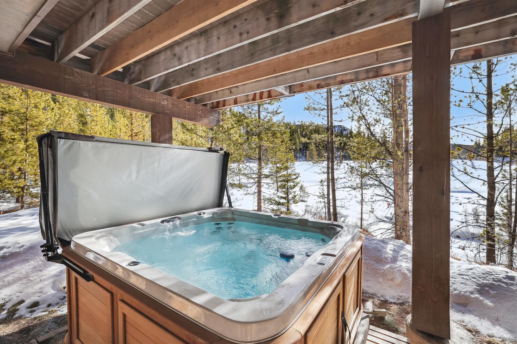 A hot tub under a wooden pergola with a snowy landscape in the background.