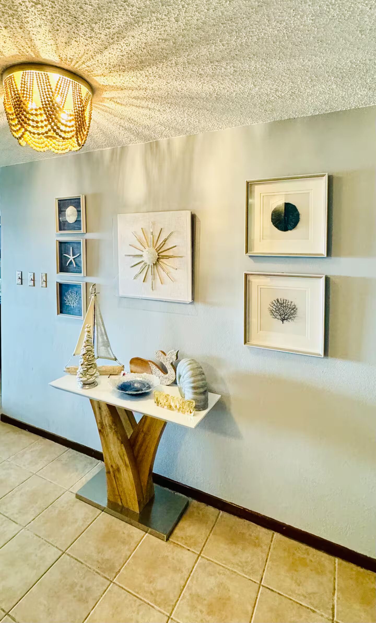 A hallway with a wooden table displaying decorative items, framed artwork on the wall, and a textured ceiling light fixture.