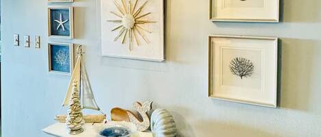 A hallway with a wooden table displaying decorative items, framed artwork on the wall, and a textured ceiling light fixture.