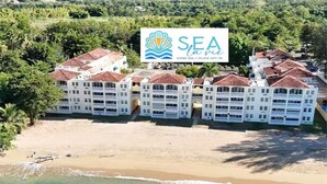 Un hôtel situé en bord de mer, composé de plusieurs bâtiments blancs, avec une plage de sable fin et une eau turquoise.