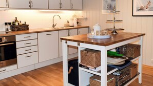 A modern kitchen with white cabinets, a Bosch oven, a wooden countertop, and a white storage cart with baskets. - 5 Star Holiday Home in Engelsviken (Fredrikstad)