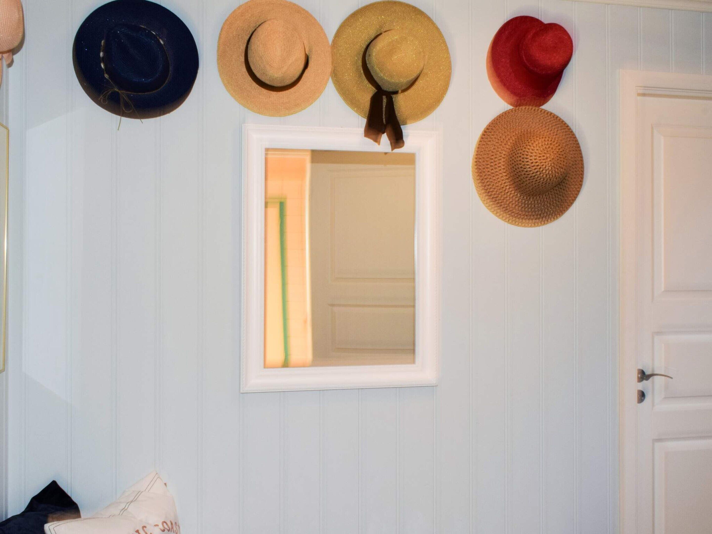 Una pared con un espejo y cinco sombreros colgados encima.