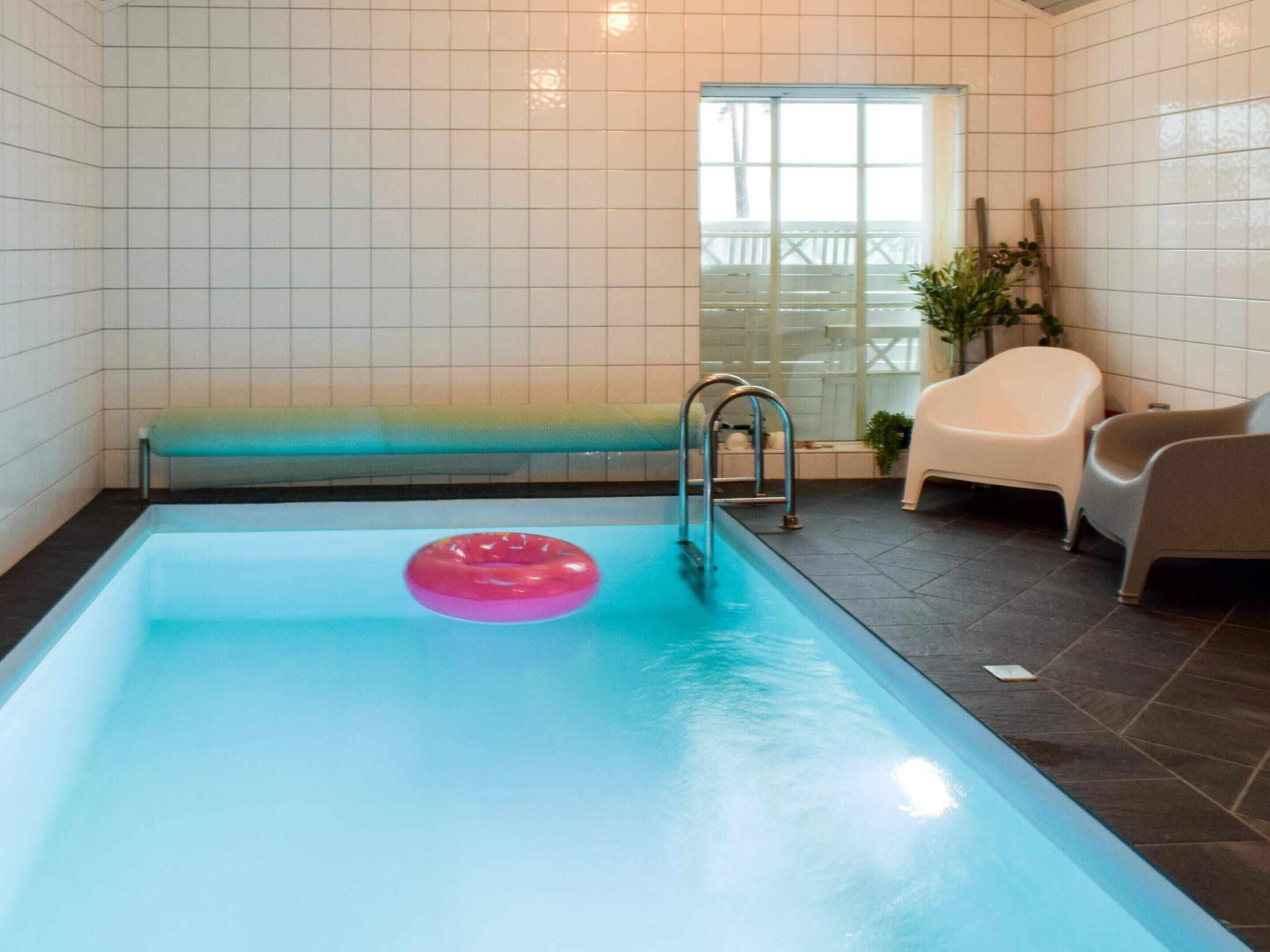 A swimming pool with a pink float, a window with a view, and a chair by the pool.