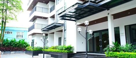 A multi-story building with a modern design, featuring balconies, large windows, and a covered entrance area.