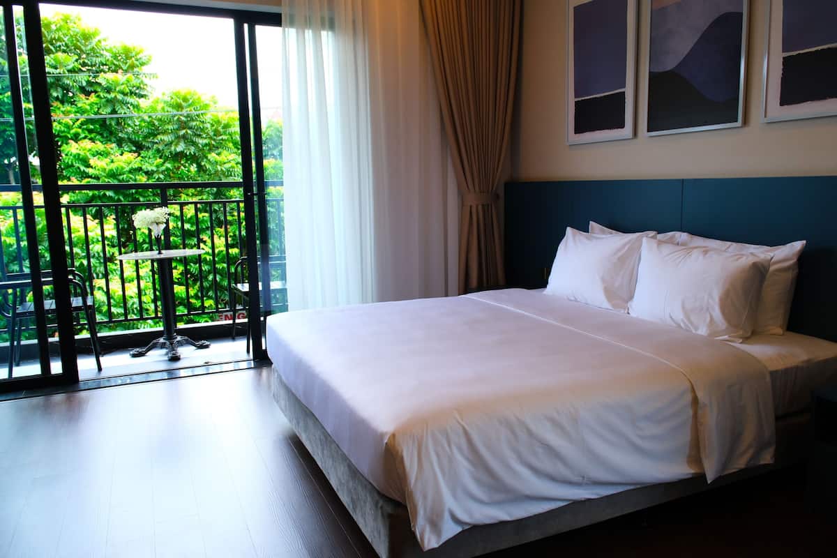 A hotel room with a large bed, a balcony with a view of greenery, and a ceiling with artwork.