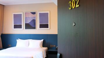 Quarto de hotel com uma cama, uma porta com o número 302 e três quadros na parede.