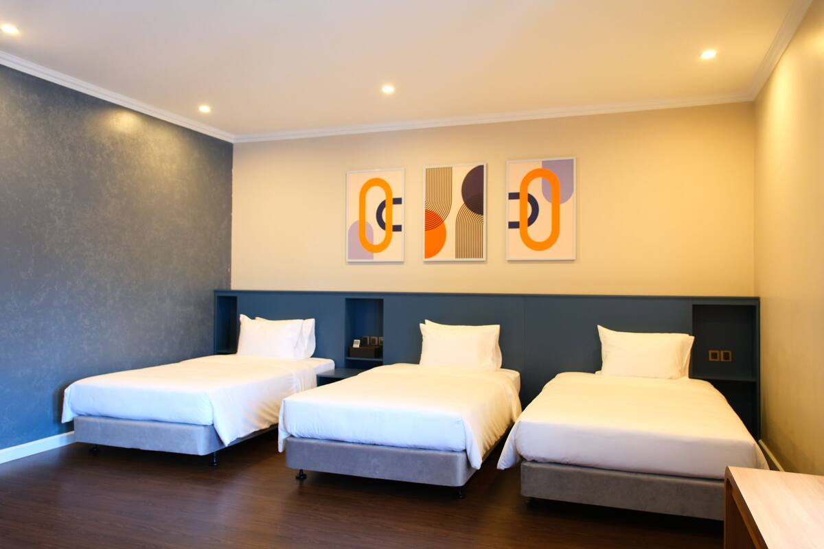 A hotel room with three single beds, a dark blue headboard, and a wall-mounted artwork.