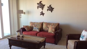 Ein Wohnzimmer mit einem roten Sofa, einem Holztisch und einem braunen Sessel. An den Wänden befinden sich dekorative Elemente und eine Lampe.