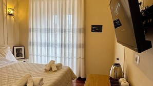 Ett hotellrum med en säng, ett träbord vid sängen, en tv som är monterad på väggen och ett fönster med gardiner.