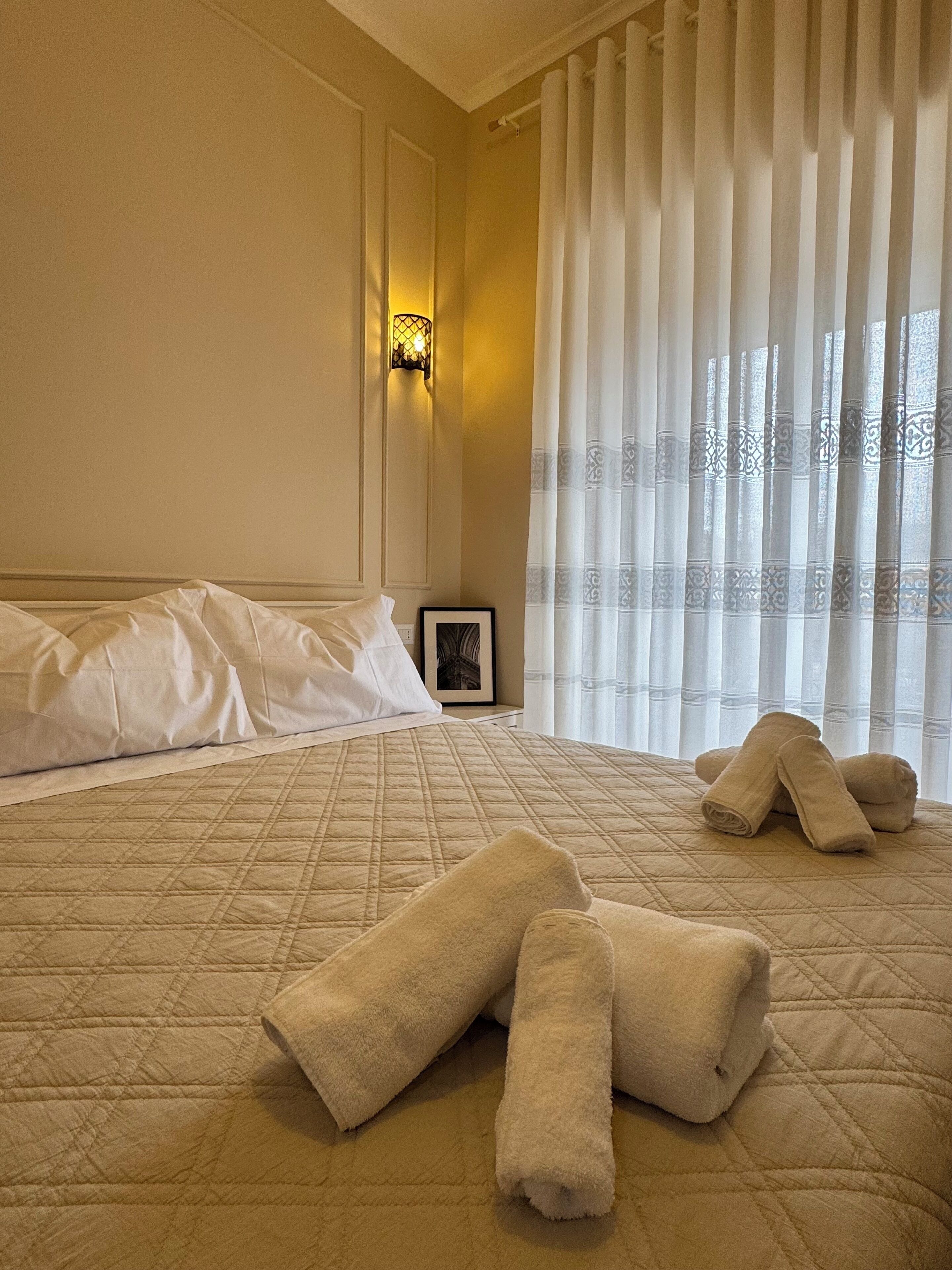 A hotel room with a bed, pillows, a framed picture, and a window with curtains.