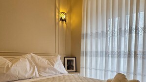 Ett hotellrum med en säng, kuddar, en inramad tavla och ett fönster med gardiner.