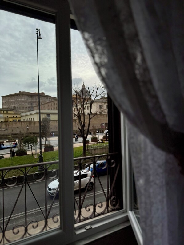 A view through a window with a metal railing, featuring a large building with a dome and a river with boats.