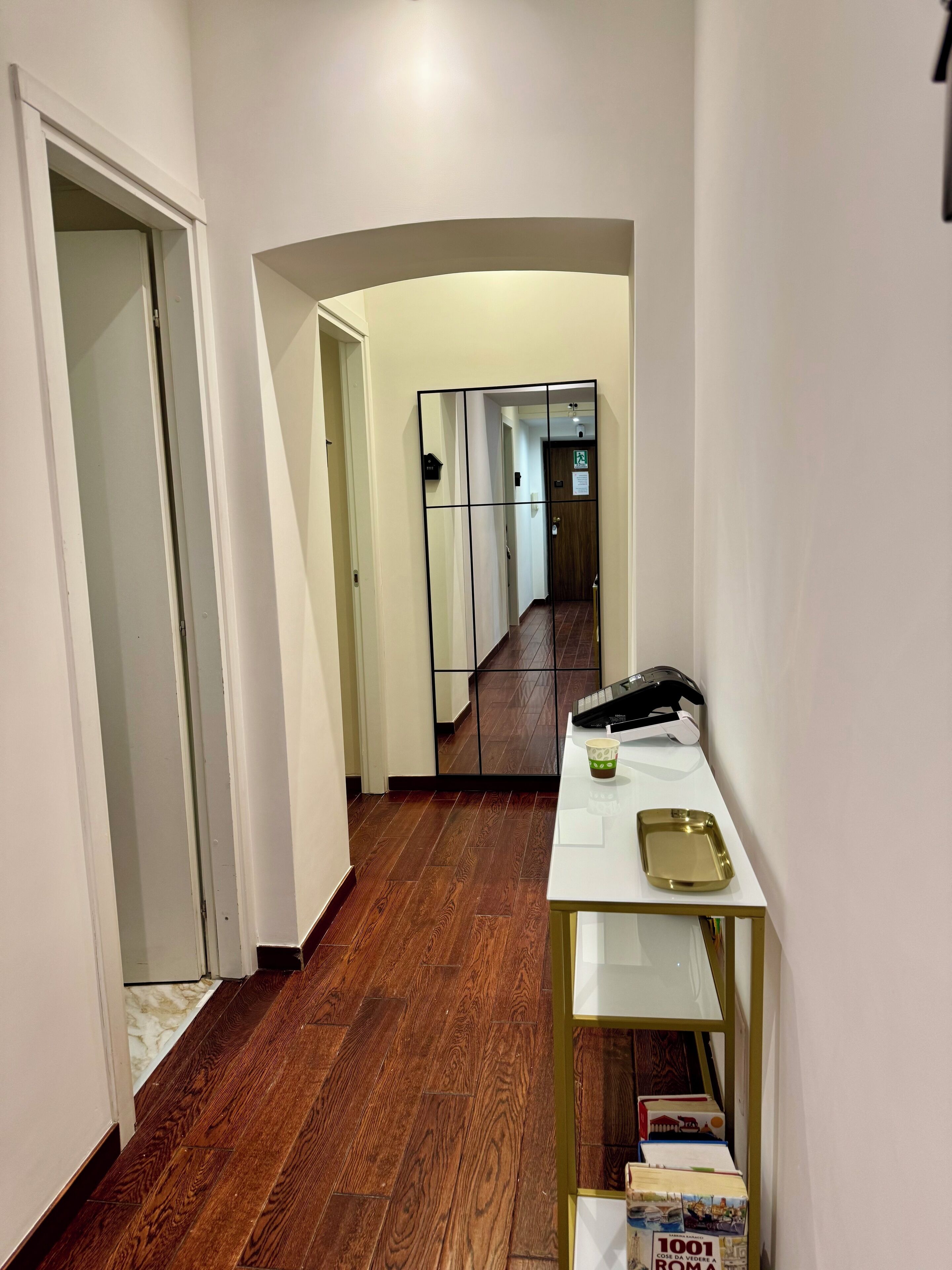 A hallway with a wooden floor, a white wall, and a white door on the left. There is a white table with a tray and a black telephone on it.