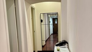 En hall med trägolv, en vit vägg och en vit dörr på vänster sida. Där står ett vitt bord med ett bricka och en svart telefon på.