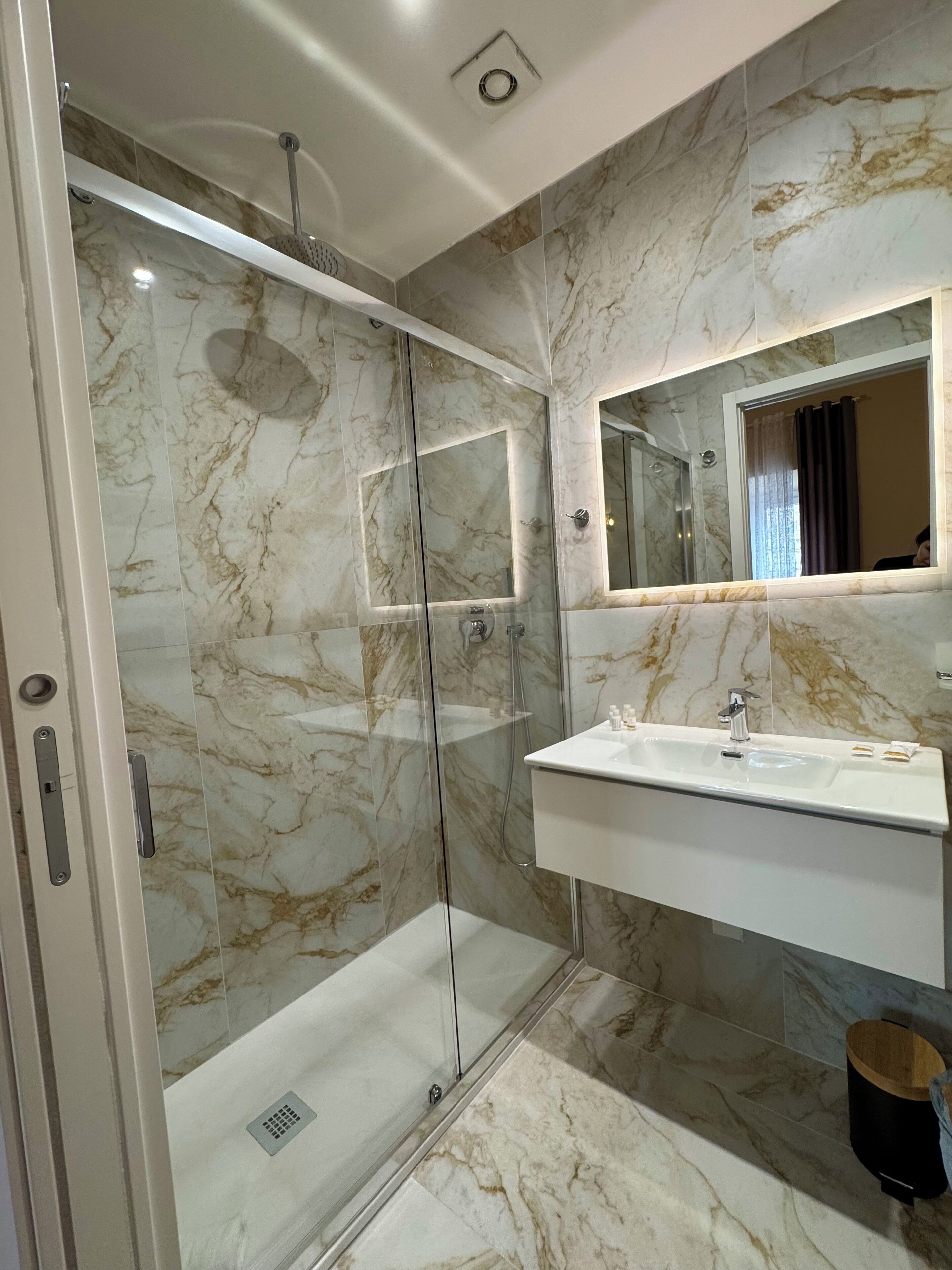 A modern bathroom with a glass-enclosed shower, a white sink, and a marble backsplash.