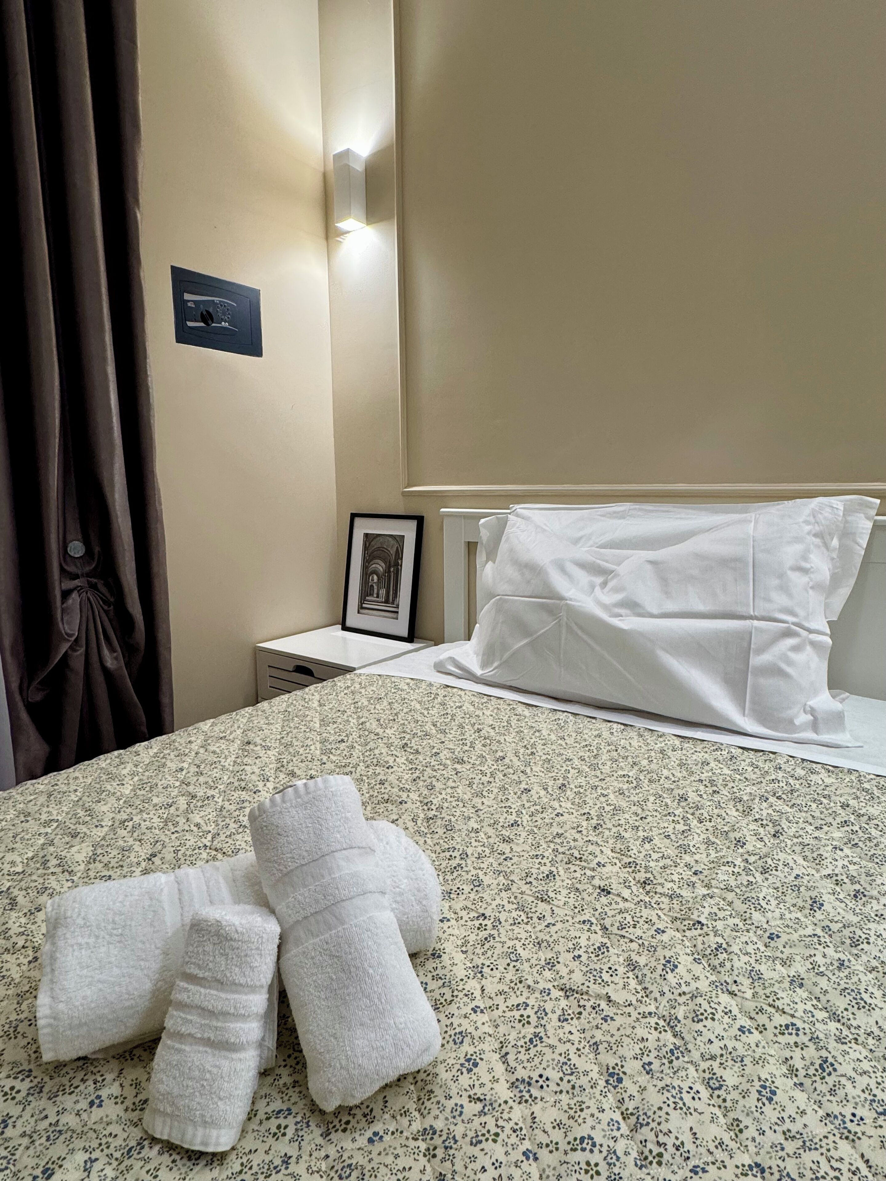 Quarto de hotel com cama, mesa de cabeceira, quadro emoldurado e luminária na parede.