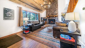 A cozy living room with a stone fireplace, a leather sofa, and a large window. - Walk Into National Park! River Access & Fishing (Estes Park)