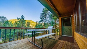 A wooden deck with a picnic table and grill, overlooking a forested area. - Walk Into National Park! River Access & Fishing (Estes Park)