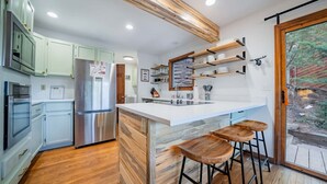 A modern kitchen with a central island, bar stools, and a view of the outdoors. - Walk Into National Park! River Access & Fishing (Estes Park)
