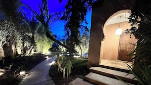 Un sendero conduce a la entrada de un edificio con escalones y una puerta, rodeado de árboles e iluminado por luces en el suelo.