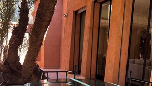 Un área de piscina con suelo de mármol, palmeras y un edificio con ventanas amplias.