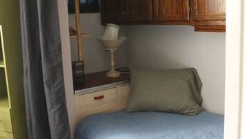 A small, single-bed room with a wooden cabinet above the bed, a bedside table with a lamp, and a green wardrobe.