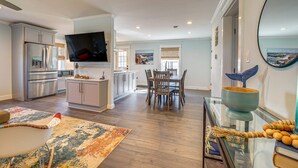 A modern kitchen with a flat-screen TV, a dining area with wooden chairs, and a large mirror reflecting a coastal view. - Peaceful Getaway Close to Loop, Beach, Dining (Wrightsville Beach)