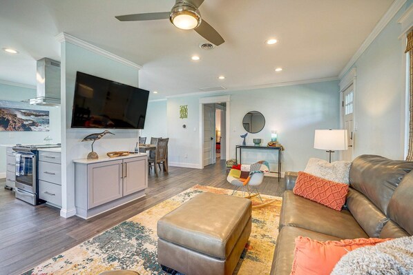 A modern living room with a leather sofa, ottoman, and a dining area with a TV and kitchen counter.