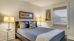 A bedroom with a bed, two bedside lamps, a framed picture above the bed, and a window with blinds. - Peaceful Getaway Close to Loop, Beach, Dining (Wrightsville Beach)