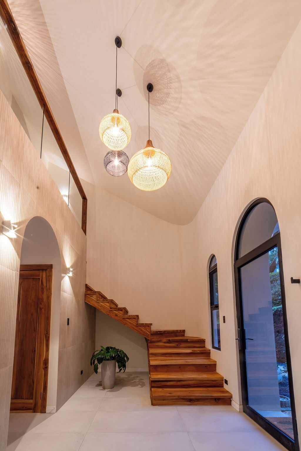 A spacious interior with a wooden staircase, a large potted plant, and three hanging spherical light fixtures.