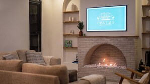 Un salon chaleureux avec une cheminée, un canapé et un écran de télévision affichant la mention « Casa Lalo, location de vacances de luxe ».