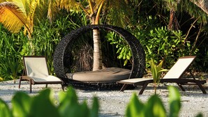 A tropical outdoor area with a circular seating area, surrounded by lush greenery and palm trees.
