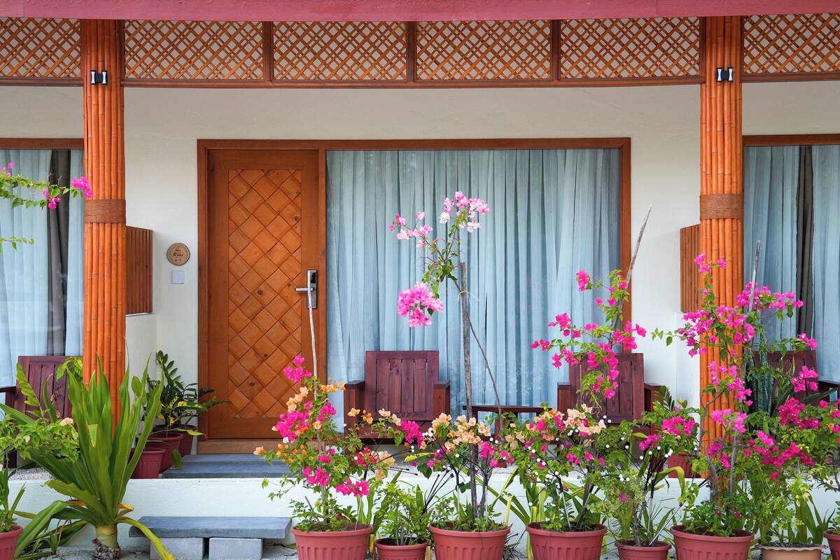 Una entrada tradicional al estilo japonés con puerta de madera, plantas en macetas y celosía de bambú.