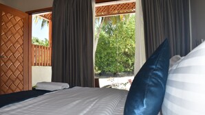 A hotel room with a bed, curtains, and a view of greenery outside.
