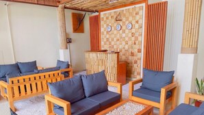 A room with wooden furniture, including sofas and a coffee table, arranged around a central area with a bamboo wall and clocks.