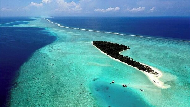 An aerial view of a tropical island with clear turquoise waters, a sandy beach, and a dense forested area.