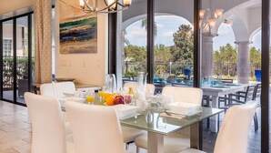 A dining area with a glass table, white chairs, and a view of the outdoors through large windows.