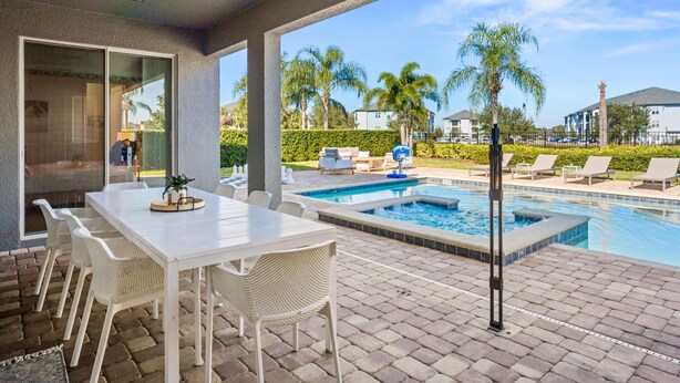 Zona junto a la piscina con mesa y sillas, un jacuzzi y vistas a palmeras y casas.