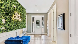 A hallway with a green wall, a neon sign, a blue sofa, and a door at the end. - Themed Bedrooms and Games Room/Private Pool and Spa/10 Mins Disney/Outdoor Chess (Kissimmee)
