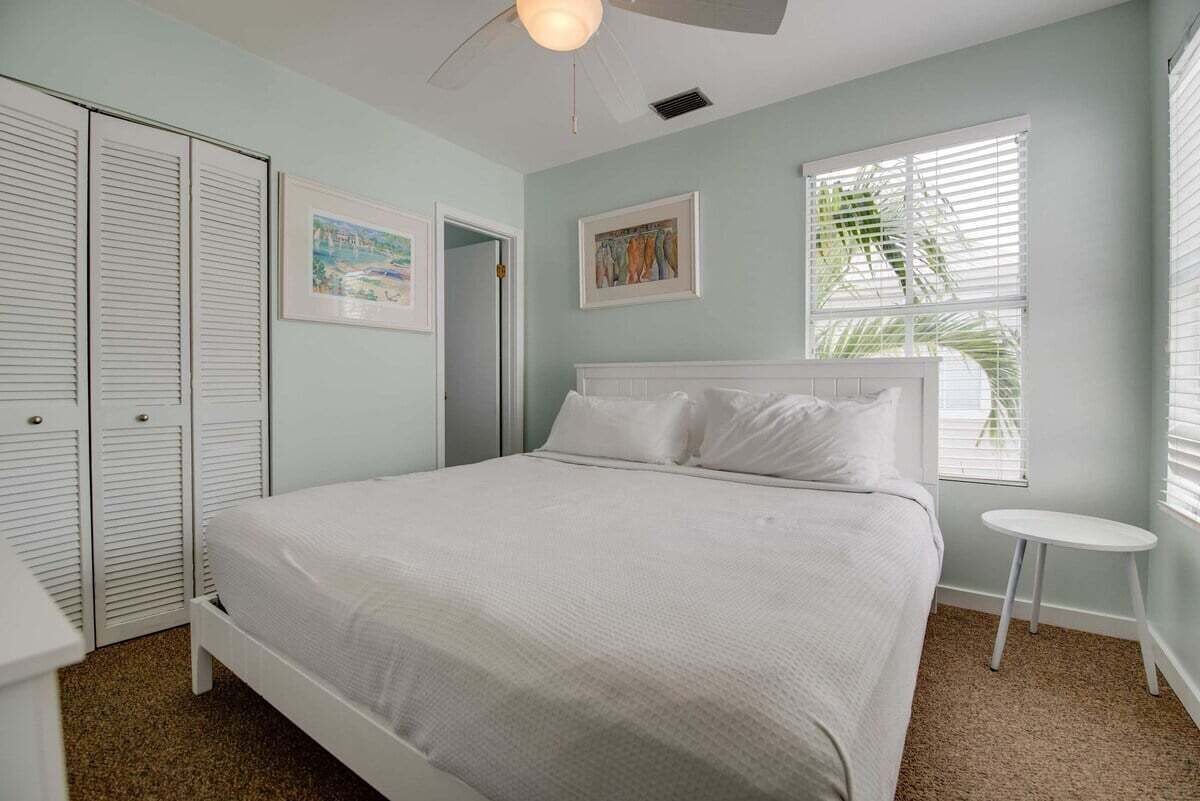 A bedroom with a bed, a ceiling fan, a window with blinds, and a door.