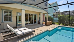 Une piscine extérieure couverte, dotée de chaises longues, d’un espace patio et offrant une vue sur une maison en arrière-plan.