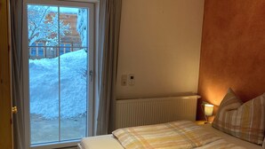 A bedroom with a wooden bed, a view of a snowy landscape through a sliding door, and a skylight above.