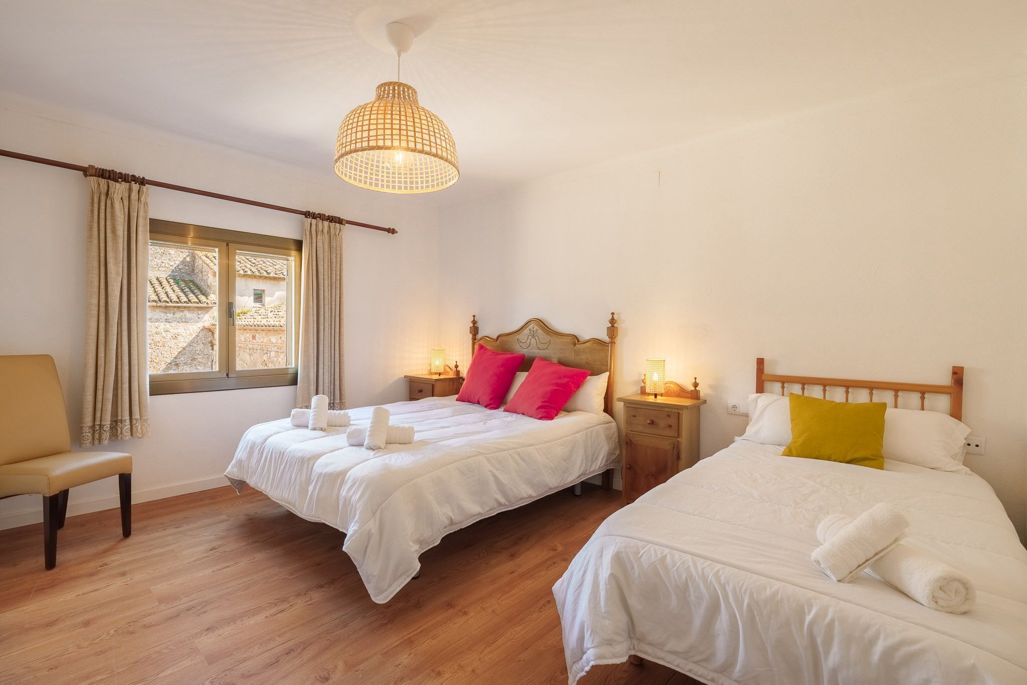 Une chambre d’hôtel avec deux lits, un banc, une fenêtre avec des rideaux et un luminaire suspendu.