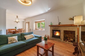 A cozy living room with a green sofa, a wooden coffee table, a fireplace, and a dining area with a table and chairs.