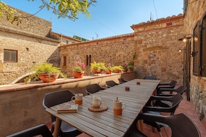 Un espace extérieur aménagé pour les repas, avec un mur en pierre, des plantes en pot et une table en bois entourée de chaises.