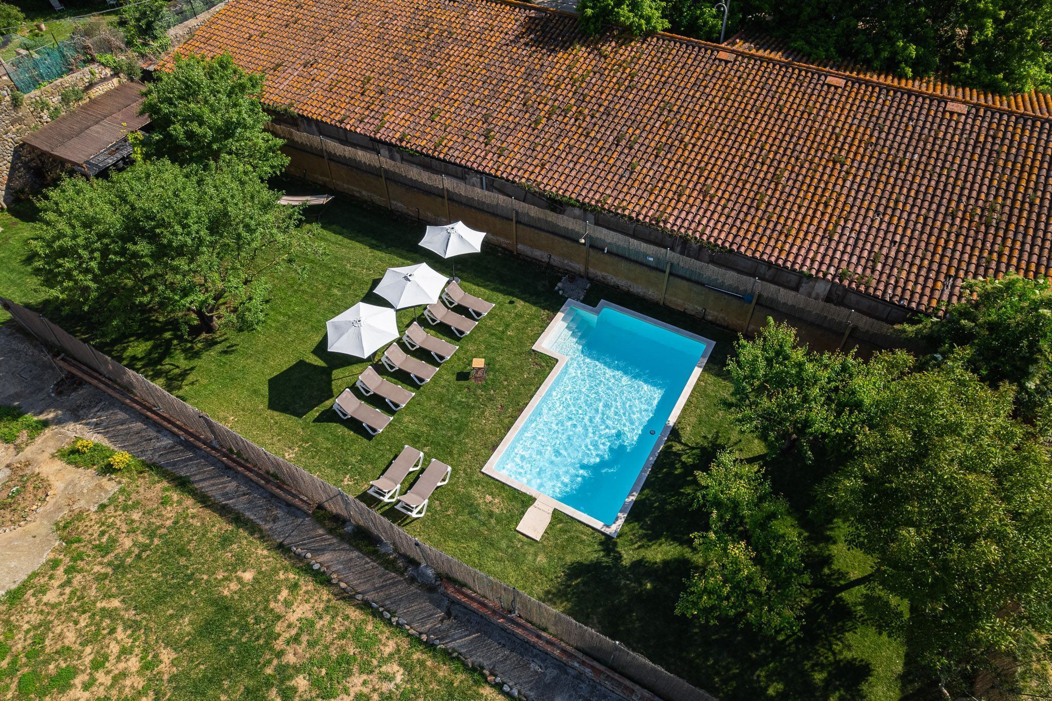 An aerial view of a property with a swimming pool, lounge chairs, umbrellas, and a tiled roof.