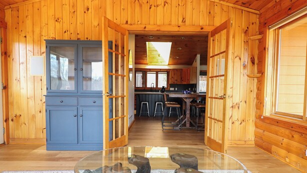 A wooden cabin interior with a dining area, kitchen, and a glass table with wooden carvings. - Cozy 3-bedroom cabin in charming Crosslake with WiFi and AC (Crosslake)